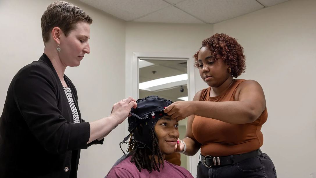 From left, Assistant Professor Rachel Romeo and Abria Simmons '25 place a fNIRS neuroimaging cap on volunteer Cole Parker.