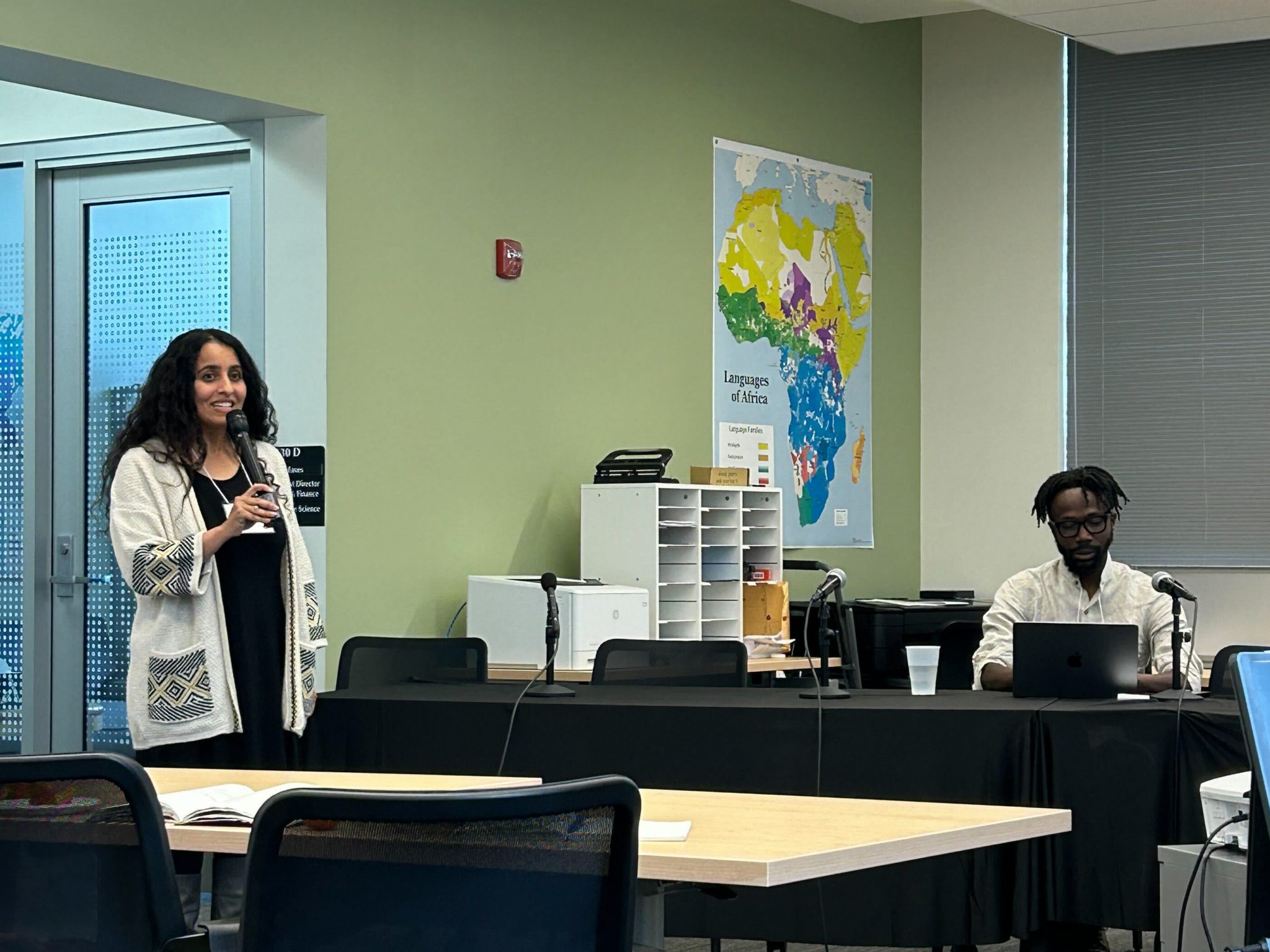 Two people, one standing with microphone and the other seated