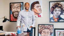 Person standing in front of art canvases with prominent African American figures